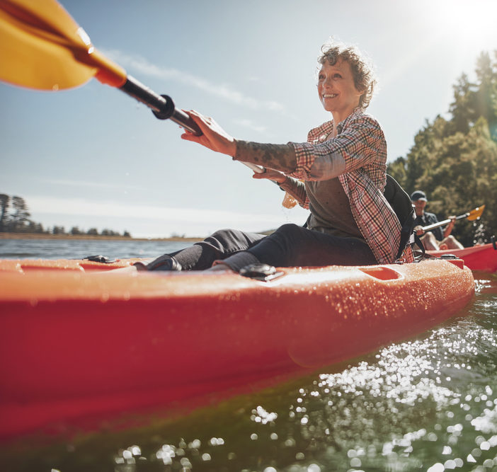 Shot of senior woman canoeing in lake on a summer day. Mature woman paddling a kayak in lake.