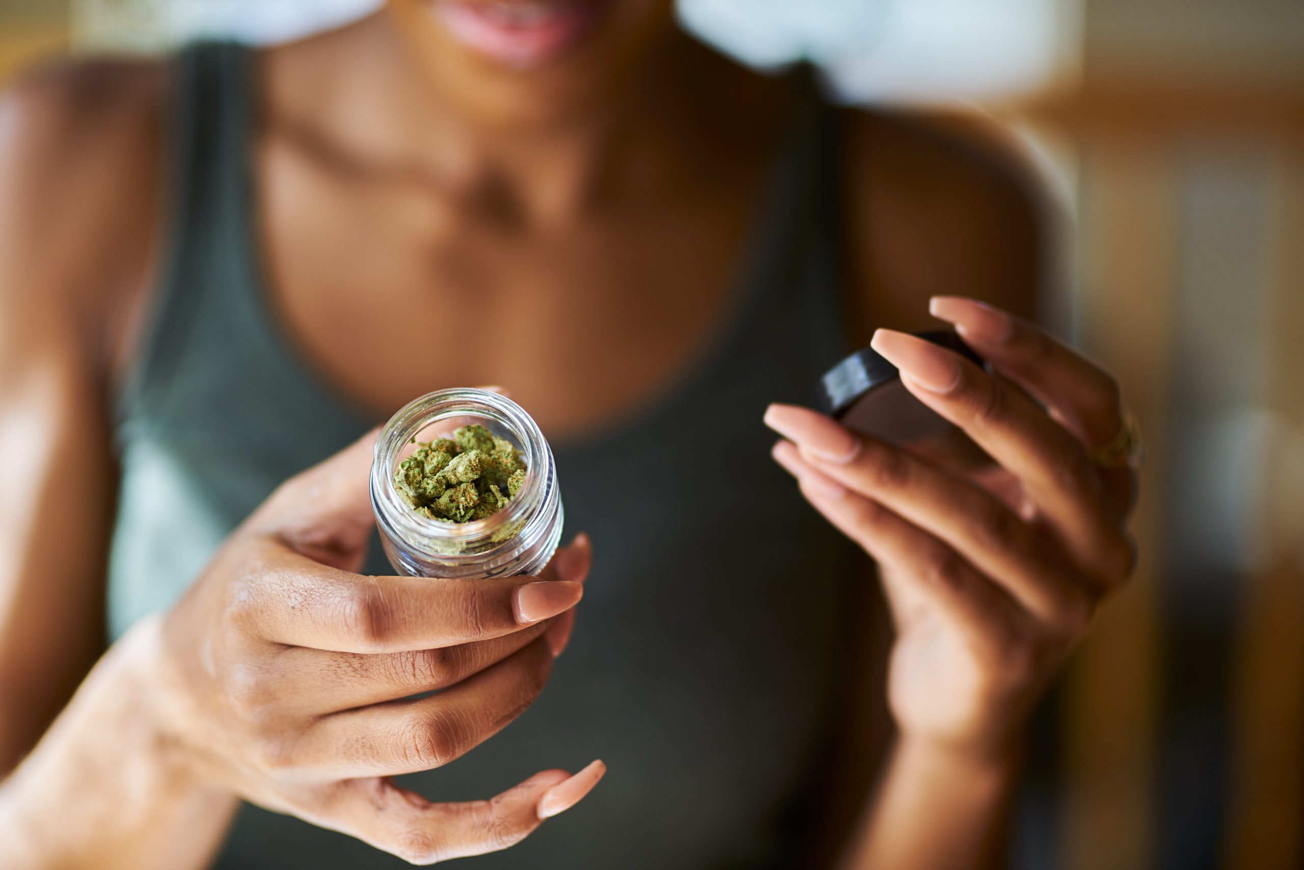 Woman of color holding out a small jar of marijuana buds.
