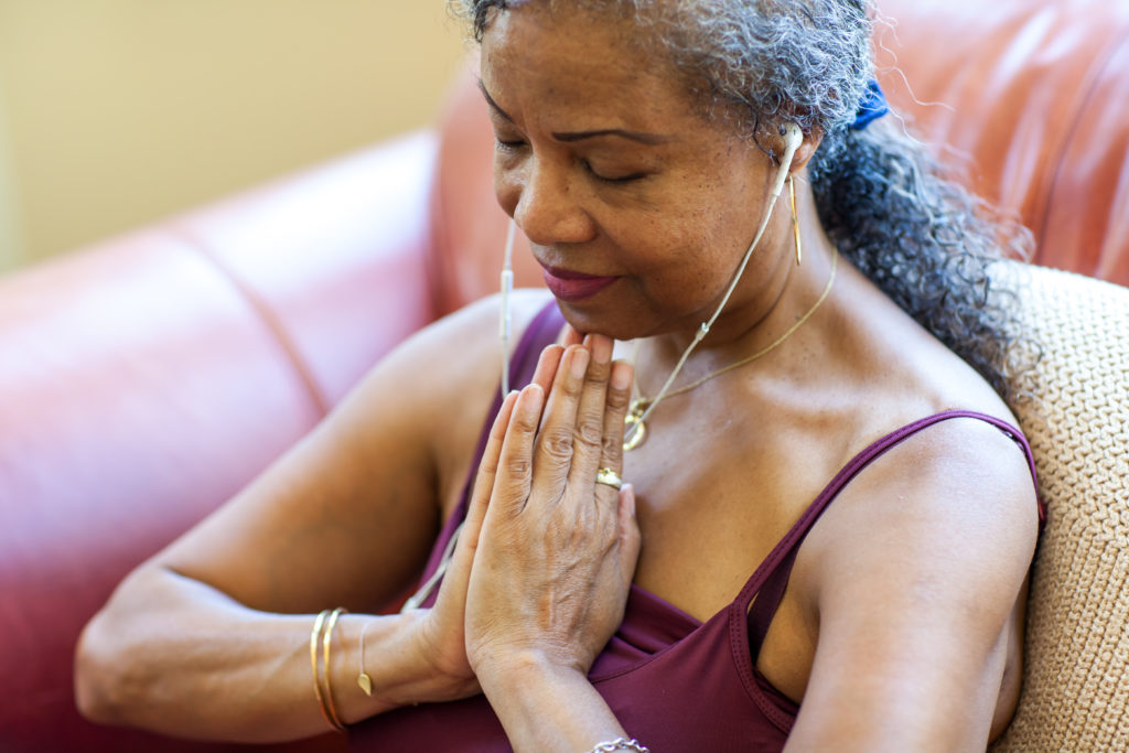Woman of colour with hands in prayer position held to her chest. She is calm and listening to music to stay centered. 
